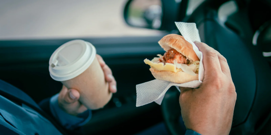 Driver holding coffee and sandwich.